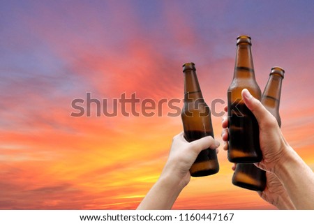 Hands holding three beer bottles and happy enjoying harvest time together to clinking glasses at outdoor party on beautiful sunset background.Celebration drinking beer.        Royalty-Free Stock Photo #1160447167