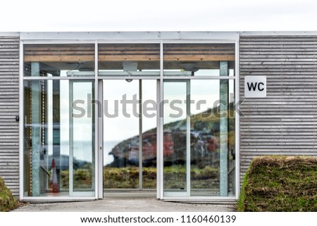 Closeup of paid WC Public Toilet building in Vik, Iceland with sign, modern glass door entrance, nobody