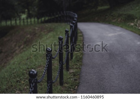 Moody, Dark Photo of the Road in a Park, Between Woods - Closeup view of the Chain Fence with Blurred Background - Desaturated, Vintage Look with Space for Text, Autumn day