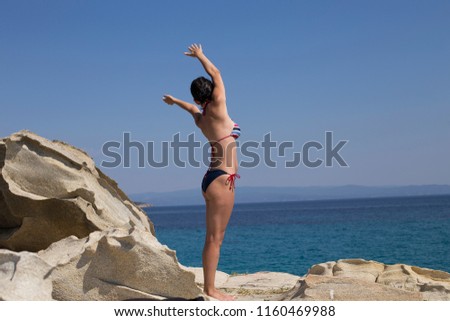 Fit beautiful woman in bikini doing stretching exercise on rocky beach, summer vacation