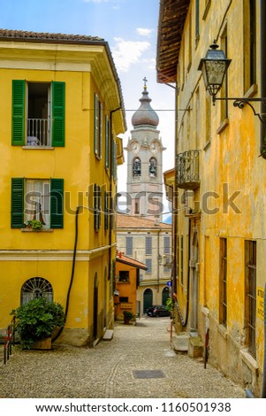 Narrow cobbled streets of Menaggio, Lake Como, Lombardy on a summers day. Looking at the spire of the Catholic Church, Santo Stefano. Royalty-Free Stock Photo #1160501938