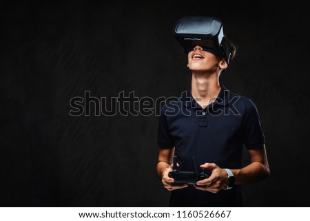 Young teenager dressed in a black t-shirt wears virtual reality glasses and controls the quadcopter using the control remote.