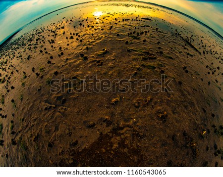A beach in Cape Cod, MA with pebbles mixing with the low tide, photographed with a fisheye lens at sunset 