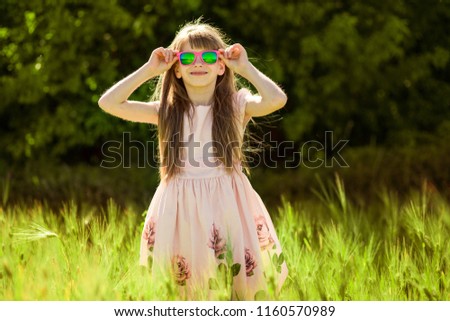 Portrait of adorable little girl in sunglasses in green summer field