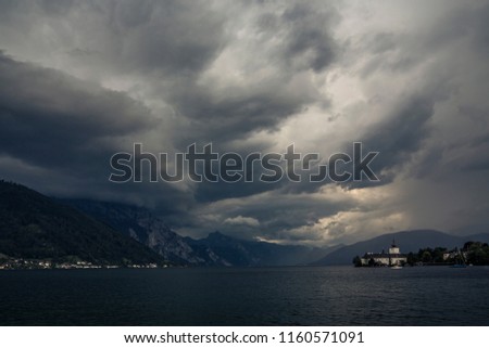Storm above Traunsee lake on panoramic photography of Ort castle in Gmunden, Salzkammergut, Austria. Dramatic cloudscape scenery from famous landmark of historic town on sea coast with must see palace
