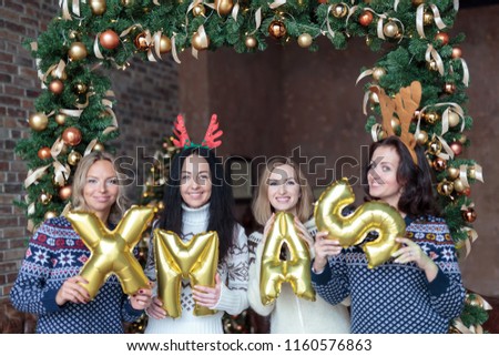 Young women holding word xmas made of golden balloons with Christmas fir tree decoration on background