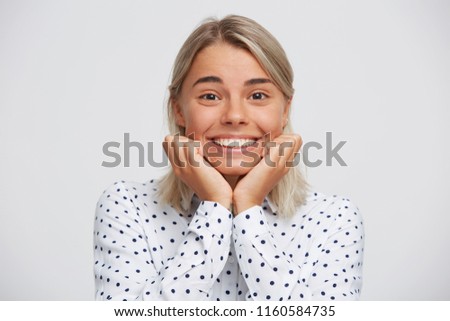 Portrait of smiling beautiful blonde young woman wears polka dot shirt feels happy and looks directly in camera isolated over white background