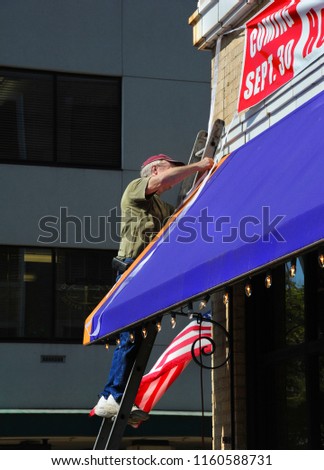 Hanging a "Grand Opening" banner, this business owner is standing on a ladder on the square in a small town in Arkansas.