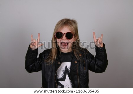 Portrait of a heavy metal little girl with sunglasses. Cute little girl making a rock-n-roll sign