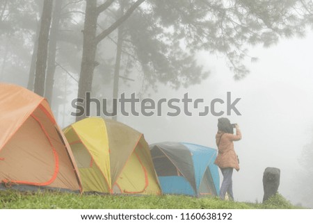 tourist take photo near tent in mist & fog. camping in pine tree forest. people, travel, vacation concept