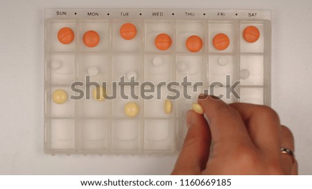 TOP VIEW: Female nurse hand puts down a pills into a pill organizer