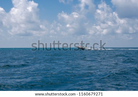A white boat racing on the sea against a blue cloudy sky.