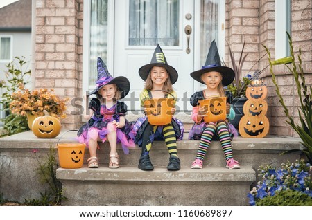 Happy Halloween! Three cute little laughing girls in witches costumes are coming to the house for sweets.
