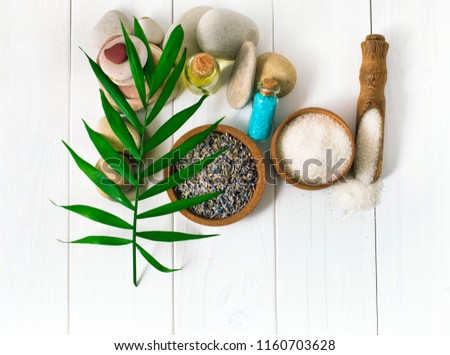 Spa background with text space. Spa stones with dry lavender flowers, white and cyan blue sea salt, green palm leaf, wooden scoop with sea salt, massage oil on white wooden background.  Top view.