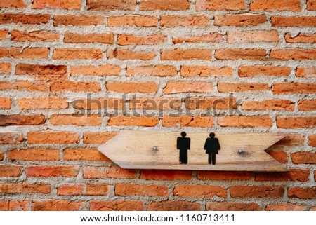 Wooden toilets sign with a male and female symbol and direction on old brick wall