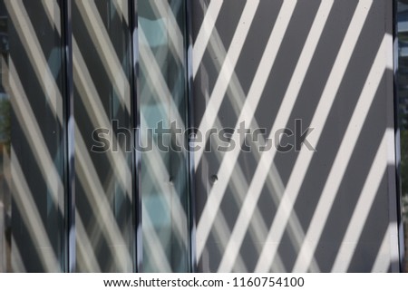 Close up view of part of glass windows in a building corner. Reflective shapes and shadows drawn on the facade. Abstract geometric design with parallel and crossing lines. Graphic image of an angle. 