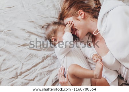 Portrait of beautiful loving mom playing first games with her 8 months old baby in bedroom, top view Royalty-Free Stock Photo #1160780554