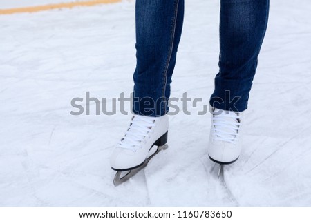 Legs of ice skater with white leather skates on ice rink, close-up view