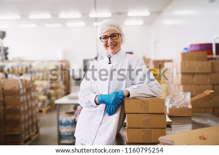 Portrait of a smiling female worker in sterile clothes leaning on a packages.