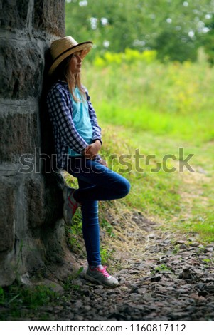 sad rural girl blonde in a hat with blue eyes near a gray wall