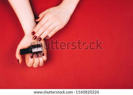 Woman holding manicure bottle on red background.