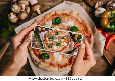 Cropped shot of food blogger taking picture of cooked pizza on baking paper on wooden surface Royalty-Free Stock Photo #1160829244