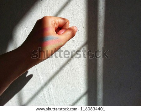 Colorful eye shadow on hands of a teenager with a shadow on the wall.