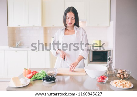 A picture of young woman cooking in kitchen. She stands and cuts vegetable. She is doing that careful.