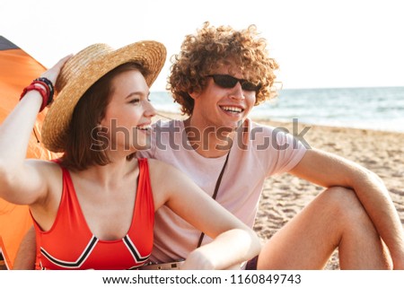 Picture of young cute loving couple friends sitting on the beach outdoors.