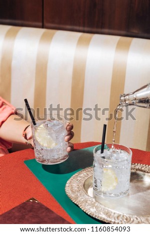 A girl holds a glass of gin and tonic while tonic water is poured, into an elegant pop-colored bar Royalty-Free Stock Photo #1160854093