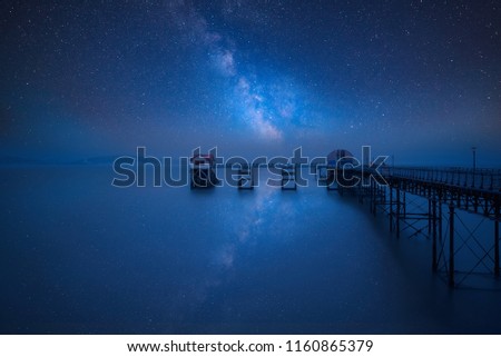 Stunning vibrant Milky Way composite image over landscape of old pier stretching out to sea