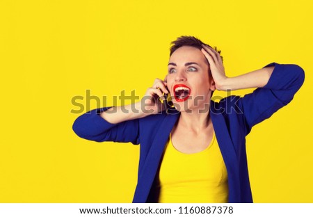 No way, omg. Good news by cell. Portrait Of Beautiful Young Woman shocked Talking On Cellphone isolated on yellow background standing on the left of the copy space. Model in yellow shirt, blue suit.