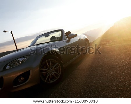 Sunset front view of silver gray convertible car, mountain valley in background Royalty-Free Stock Photo #1160893918