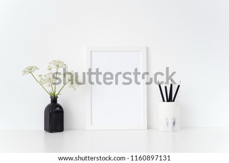 Modern white portrait a4 frame mock up with a herbal gerard in black vase and black pencils near white wall. Mockup for quote, promotion, headline, design. Template for lifestyle bloggers, social