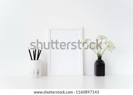 Stylish white portrait a4 frame mock up with a wild host in black vase and black pencils near white wall. Mockup for quote, promotion, headline, design. Template for small businesses, social media
