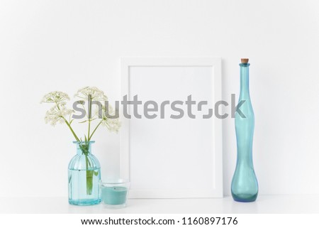 Stylish white portrait a4 frame mock up with a Aegopodium in transparent blue vases, blue candle on white background . Mockup for work. Template for small businesses, lifestyle bloggers, social media
