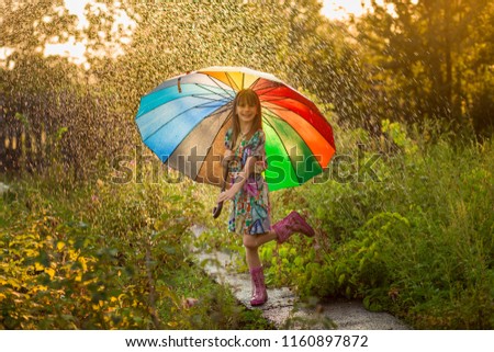 Happy child girl walk with multicolored umbrella under summer rain 