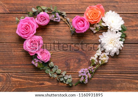 Heart made of beautiful flowers and leaves on wooden background