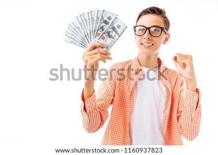 A young man in glasses enjoys a large number of bills a hundred dollars, a portrait of a successful teenager in a shirt in the Studio