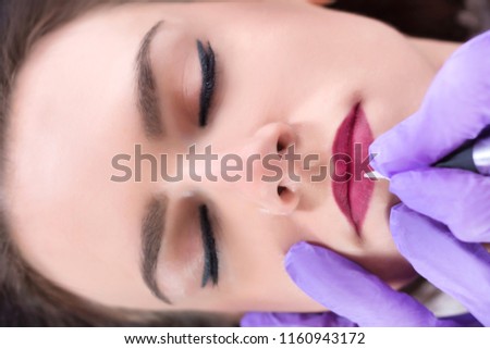 Applying red permanent make up tattoo on young girl lips in beauty salon. Modern and new make up concept. Close up, selective focus