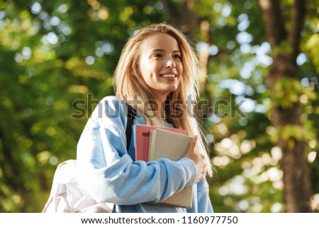 Close up of happy young girl student with backpack carrying books, walking at the park