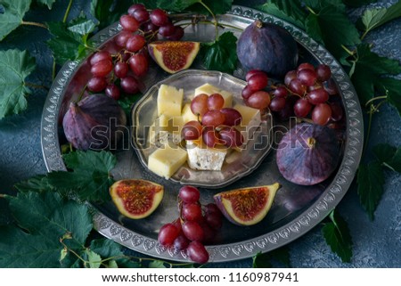 on a gray background in a silver plate red grapes, figs and cheese, around the vine