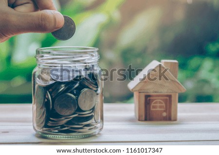 House placed on the wood. Men's hand is putting coin into jar. planning savings money of coins to buy a home concept for property ladder, mortgage and real estate investment. saving for a house,