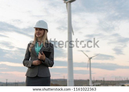 Construction business. Windmills and the object in the background. Business lady in a helmet on the background of windmills with a digital tablet is planning the construction of a new facility.