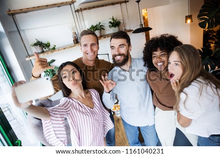 Group of friends having lunch and taking selfie with smartphone at the moder interior indoors at home together