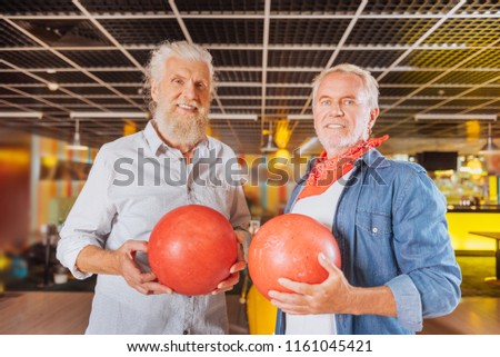 Bowling fans. Joyful nice men standing together while holding bowling ball