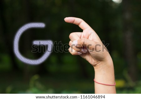 signs and symbols for people with disabilities concept of dactyl international alphabet by female hand and fingers with letter "G" on dark unfocused natural background