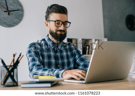 smiling young bearded developer working with laptop