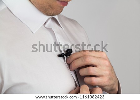 A man puts on lavalier microphone, preparation for interview, gray background