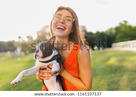 happy pretty woman park holding boston terrier dog, smiling positive mood, trendy summer style, wearing orange dress, sunglasses, playing with pet, having fun, sunny weekend entertainment